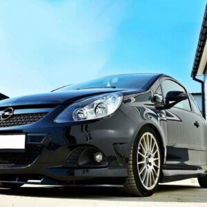 Black sporty hatchback with alloy wheels parked between white buildings on a sunny day, front angled toward the viewer.
