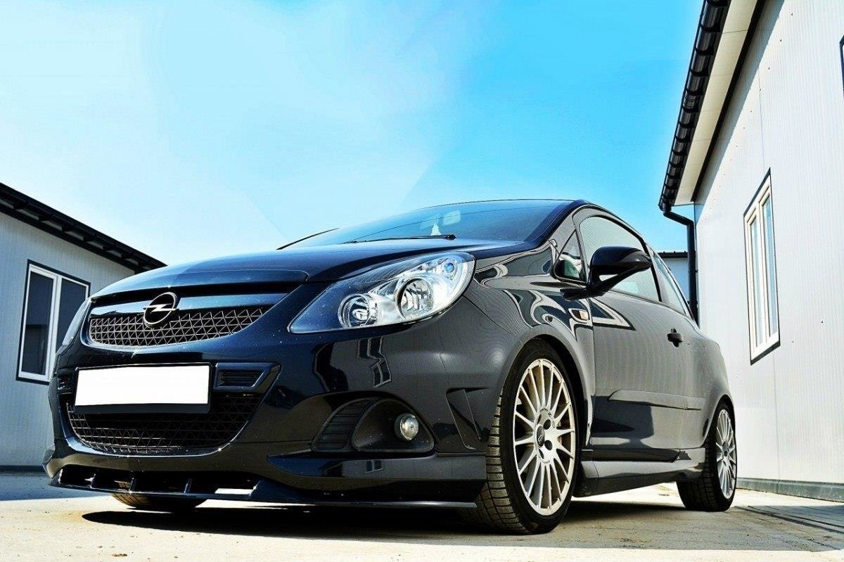 pol_po_FRONT-SPLITTER-suitable-for-Opel-CORSA-D-NURBURG-FOR-OPC-VXR-BUMPER-841_2jpg - OPSHOLDERS Black sporty hatchback with alloy wheels parked between white buildings on a sunny day, front angled toward the viewer.