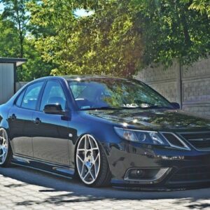 Black sedan with lowered suspension and large silver multi-spoke wheels parked on a sunny driveway.
