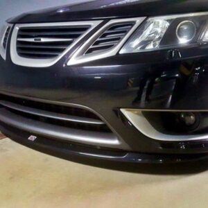 Dark sedan front view in a parking garage, showing grille, headlight, and lower bumper.