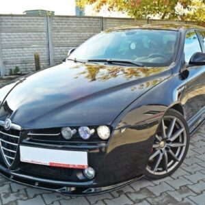 Black Alfa Romeo sedan with glossy finish and large multi-spoke wheels parked on a brick driveway against a fence.