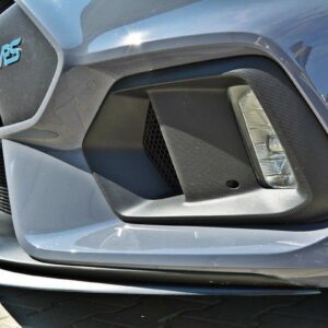 Close-up of a gray car's front bumper featuring a hexagonal grille, carbon-fiber panel, fog light, and an RS badge on the left.