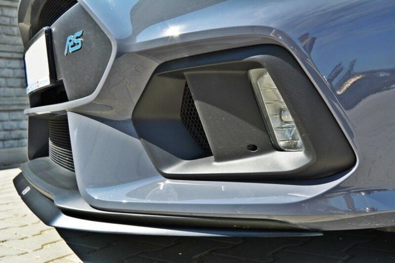 Close-up of a gray car's front bumper featuring a hexagonal grille, carbon-fiber panel, fog light, and an RS badge on the left.
