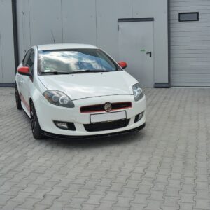White compact car with red accents parked on a gray brick lot in front of industrial gray doors and walls.