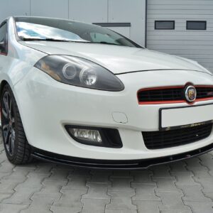 Front three-quarter view of a white Abarth sports car with red accents parked on a paved surface in front of a gray industrial building.