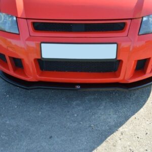 Front view of a red car with an aggressive aftermarket bumper, large lower grille, and a black front splitter on a gravel surface, license plate blanked.