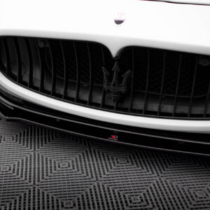 Close-up of a white Maserati front grille featuring the trident emblem on a glossy bumper, with a textured floor below