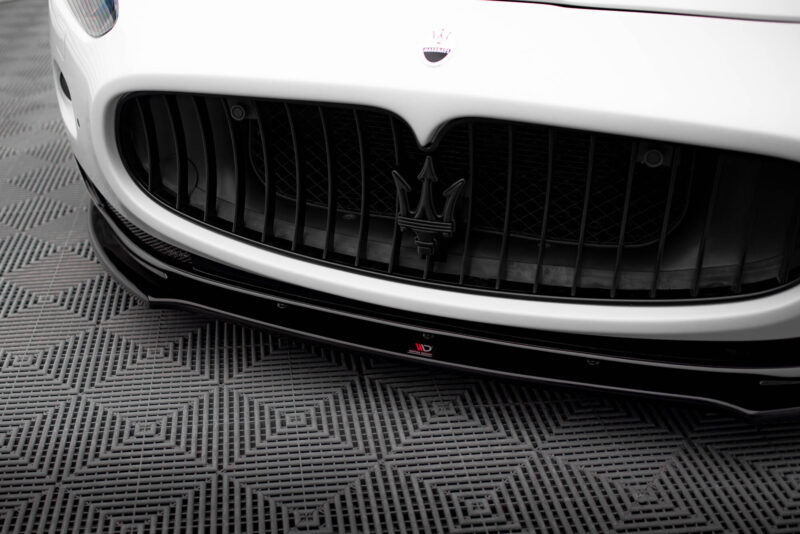 Close-up of a white Maserati front grille featuring the trident emblem on a glossy bumper, with a textured floor below