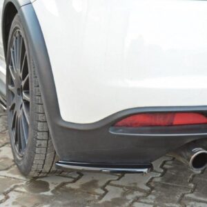 Rear of a white car showing dual chrome exhaust pipes, black bumper, and taillight on a brick-paved surface