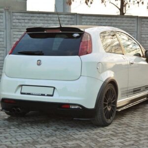 White hatchback car with black aftermarket wheels parked on a cobblestone driveway, side decals and dual exhausts visible at the rear.