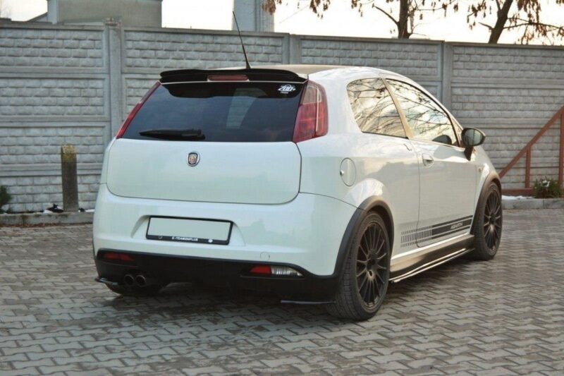 White hatchback car with black aftermarket wheels parked on a cobblestone driveway, side decals and dual exhausts visible at the rear.