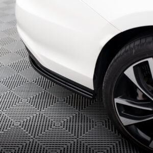 Close-up of a white car's front fender and wheel on a textured gray floor.