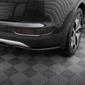 Rear view of a glossy black car showing the taillight, exhaust, and wheel on a textured showroom floor surface.