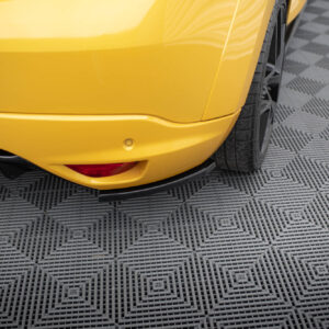 Close-up of a yellow car's rear corner showing the bumper, light, and wheel on a patterned floor.