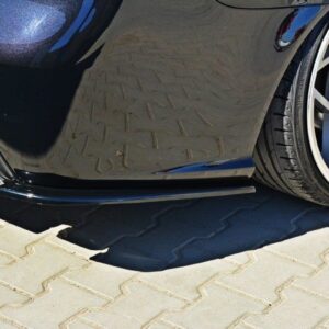 Close-up of a black sports car's rear quarter panel and silver alloy wheel on a brick-paved surface.