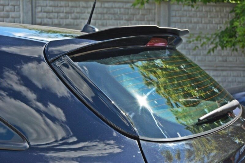Rear window of a dark blue car showing a wiper blade and a small spoiler, with reflections of trees and sky in the glass.