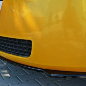 Close-up of a yellow car's front bumper showing a black grille, lower chrome lip, and a tire visible on the right.