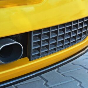 Close-up of a yellow car's front bumper showing a round exhaust pipe beside a black ventilated grille.