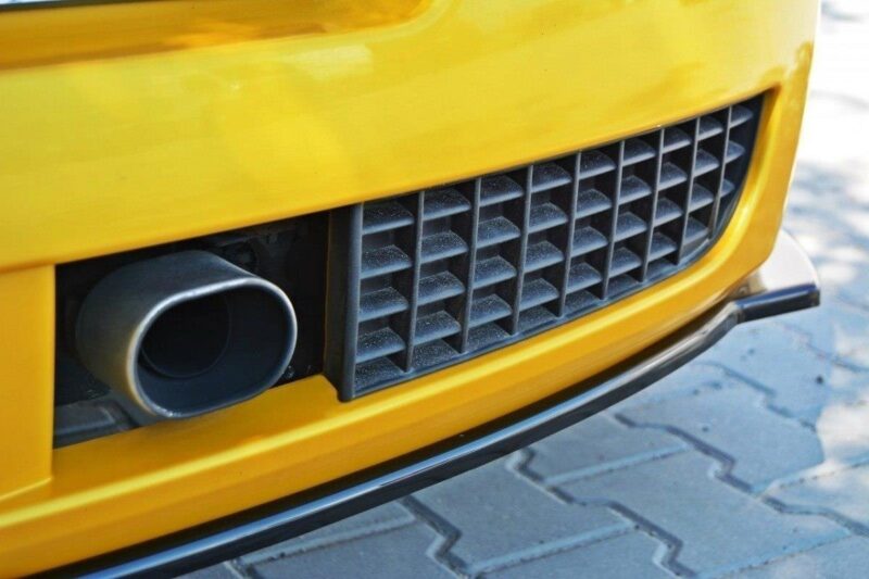 Close-up of a yellow car's front bumper showing a round exhaust pipe beside a black ventilated grille.