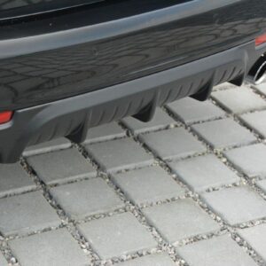 Rear of a dark car showing twin exhaust pipes and a ridged diffuser on a paved surface.