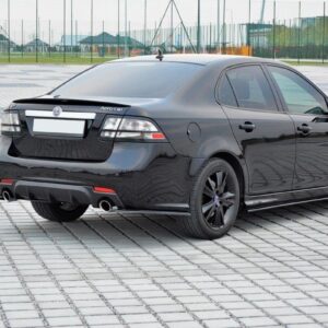 Rear three-quarter view of a black four-door sedan parked on a patterned paved area with a sports field in the background.