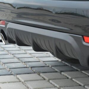 Close-up of the rear bumper of a dark car with two chrome exhaust tips and a sculpted diffuser, parked on a paved surface.