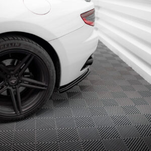 Rear left side of a white car showing a black alloy wheel with a Michelin tire, in a showroom with a patterned floor.