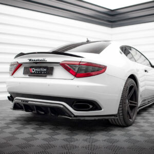 Rear three-quarter view of a white Maserati sports car in a studio with a striped wall, showing the Maserati badge and Maxton Design plate.