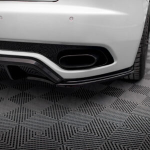 Close-up of a white car's rear bumper showing a black exhaust outlet and round parking sensors