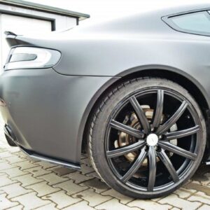 Rear-side view of a gray sports car with a large black multi-spoke alloy wheel and visible brake disc on a paved driveway/lot.