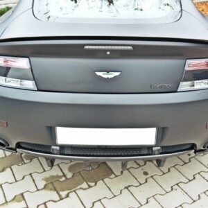 Rear view of a matte gray Aston Martin Vantage, showing taillights, emblem, and rear diffuser on a brick-paved surface.