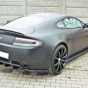Rear three-quarter view of a matte gray Aston Martin Vantage with large black alloy wheels parked on a brick driveway.