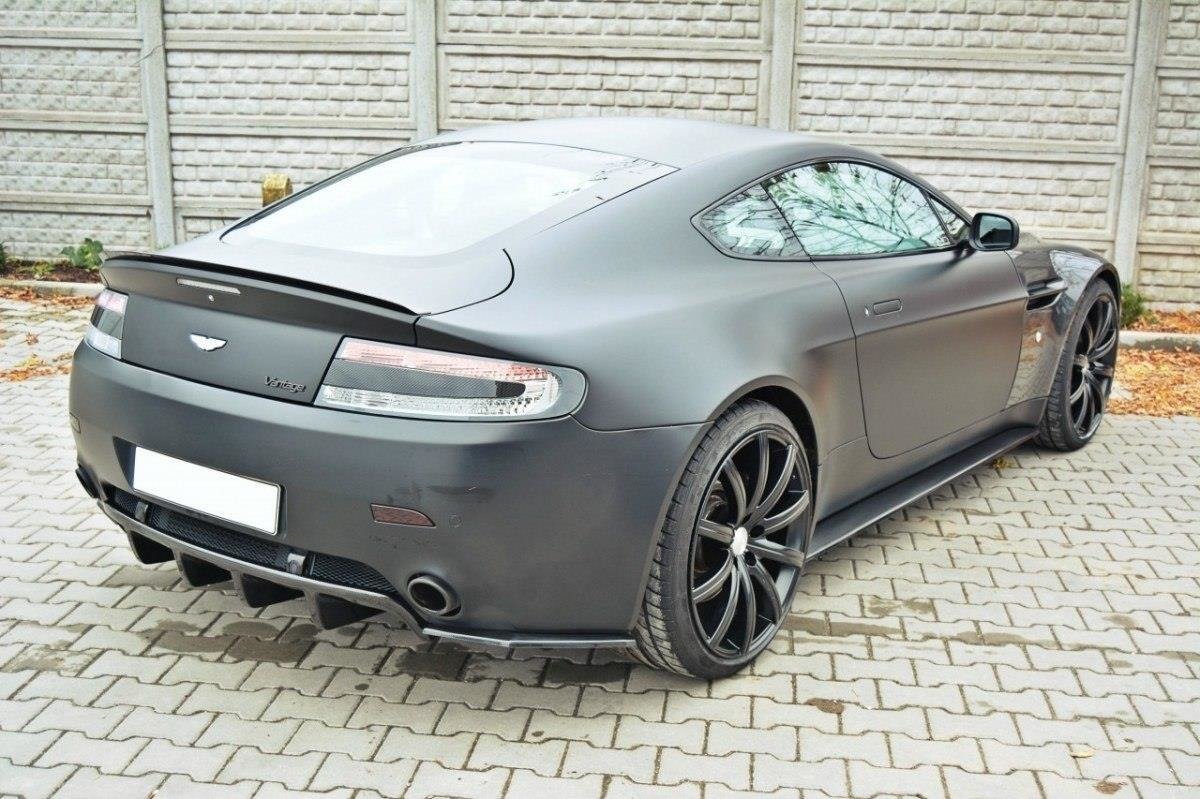 Rear three-quarter view of a matte gray Aston Martin Vantage with large black alloy wheels parked on a brick driveway.
