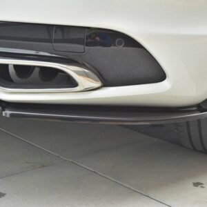 Close-up of a white car's rear bumper showing dual oval exhaust outlets with chrome trims and a black diffuser panel, parked on concrete tiles.