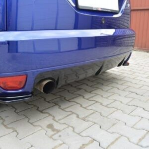 Rear view of a blue car showing a large exhaust tip and red rear reflector on a brick-paved driveway.
