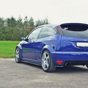 Blue Ford Focus RS hatchback parked on an asphalt surface with grassy field and trees in the background, seen from rear three-quarter view.