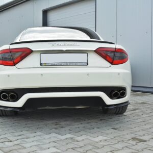 Rear view of a white Maserati parked in front of a gray industrial building with closed garage doors.