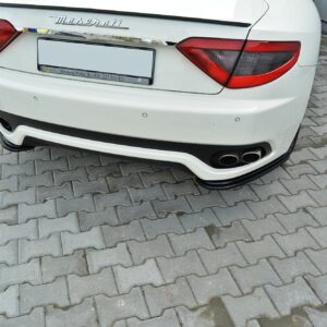 White Maserati rear view parked on gray interlocking pavers, showing taillights, chrome badge and quad exhausts in the bumper