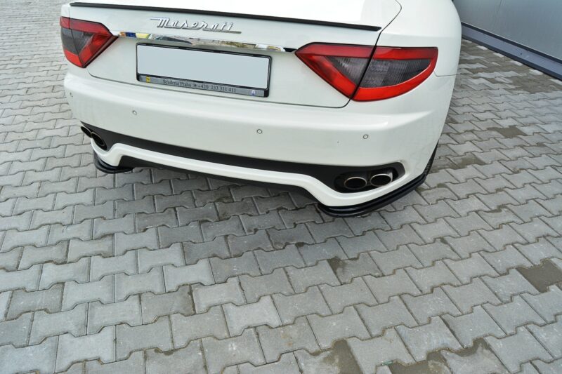 White Maserati rear view parked on gray interlocking pavers, showing taillights, chrome badge and quad exhausts in the bumper
