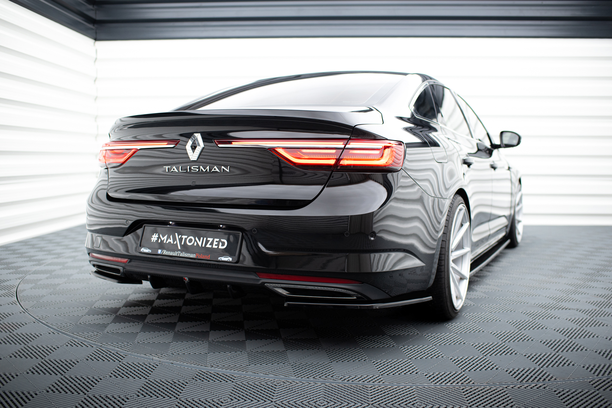 pol_po_Rear-Side-Splitters-suitable-for-Renault-Talisman-1143_2jpg - OPSHOLDERS Rear view of a glossy black Renault Talisman in a bright showroom, with distinctive red taillights and the Renault diamond badge visible on the trunk.