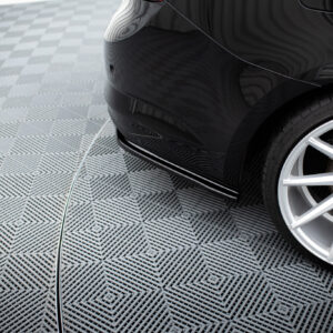 pol_po_Rear-Side-Splitters-suitable-for-Renault-Talisman-1143_4jpg - OPSHOLDERS Close-up of a black car's rear quarter, halogen wheel and tire visible on a patterned metal floor with a white cord lying on the ground.