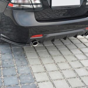 Rear view of a black car with dual chrome exhaust pipes and a textured rear bumper on a paved driveway surface.