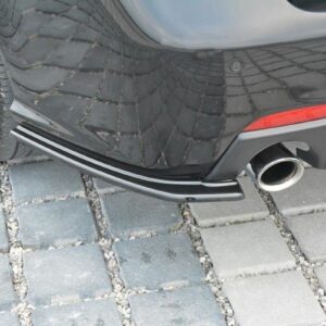 Rear view of a black car showing a chrome exhaust tip and bumper on a gray paving stone surface.