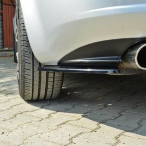 Rear view of a silver car showing a circular exhaust pipe near the bumper, parked on a brick-paved driveway.