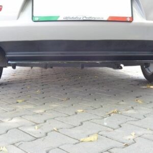 Rear view of a car showing the exhaust pipe on the left and the lower bumper, parked on a paved area with fallen leaves nearby.