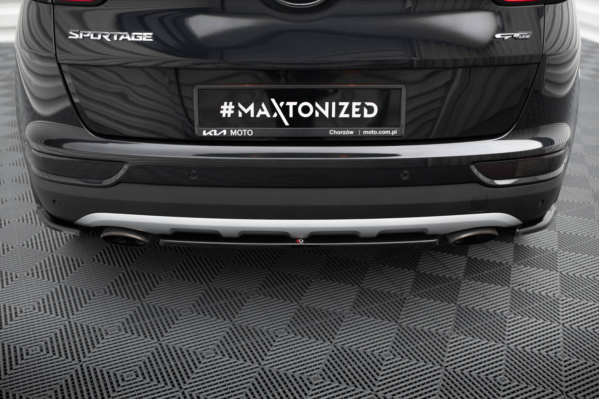 Rear view of a black Kia Sportage with a custom plate reading '#MAXTONIZED' and 'KIA MOTO' branding beneath it.