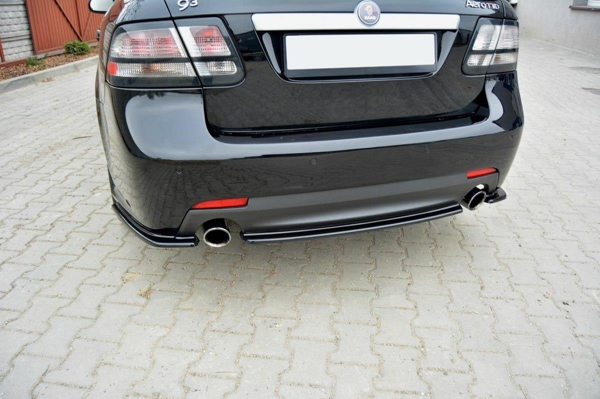 pol_po_Rear-Splitter-suitable-for-Saab-9-3-Aero-Mk2-Facelift-1054_1jpg - OPSHOLDERS Rear view of a black sedan on a brick-paved driveway, showing two chrome exhaust pipes and a blurred license plate area.