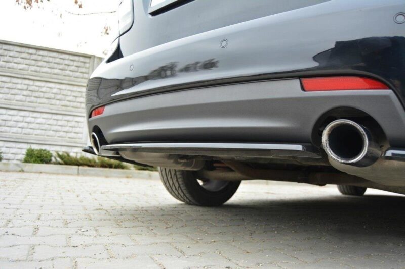 pol_po_Rear-Splitter-suitable-for-Saab-9-3-Aero-Mk2-Facelift-1054_5jpg - OPSHOLDERS Rear of a silver car showing a large circular exhaust tip on the right side of the bumper, parked on a brick-paved driveway beside a stone wall.