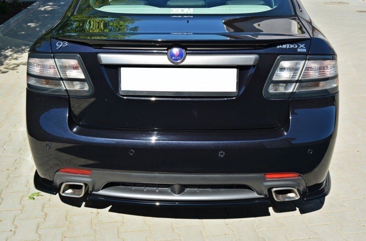 pol_po_Rear-Splitter-suitable-for-Saab-9-3-TURBO-X-1055_2jpg - OPSHOLDERS Rear view of a dark Saab 9-3 Turbo X parked on a paved surface, showing taillights, license plate area, and dual exhausts with chrome tips.