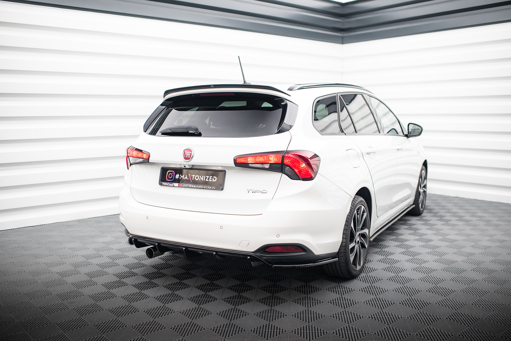 pol_po_Rear-Valance-suitable-for-Fiat-Tipo-S-Design-SW-5801_4jpg - OPSHOLDERS Rear view of a white Fiat hatchback in a bright showroom, showing taillights, rear window wiper, and spoiler against white walls and patterned floor.